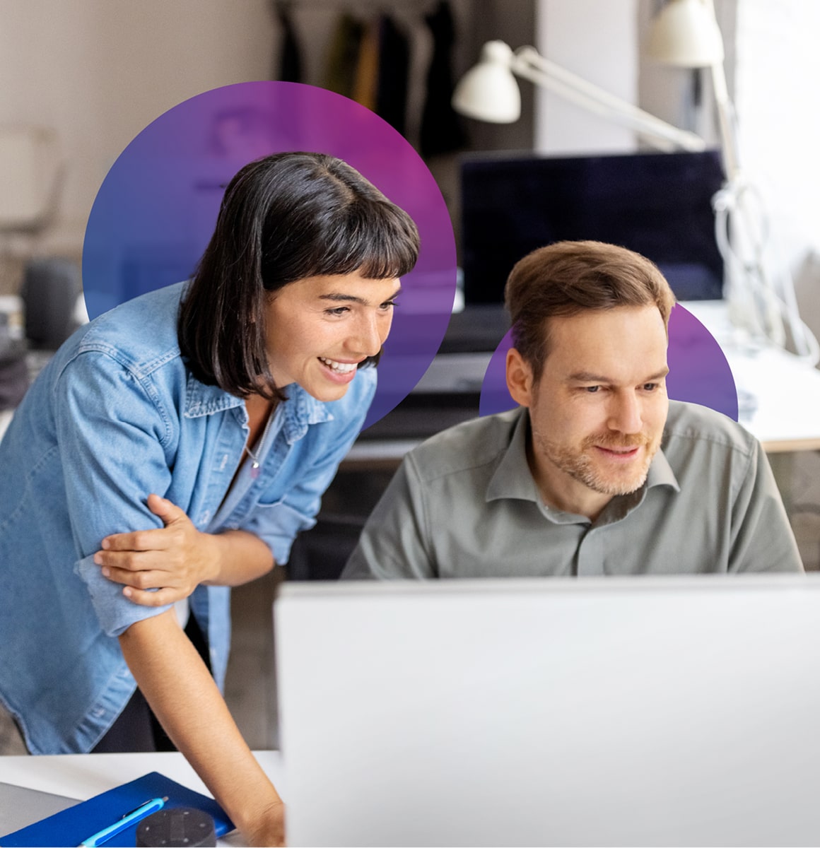 Two colleagues gathered at a desk, reviewing something on a computer screen together.