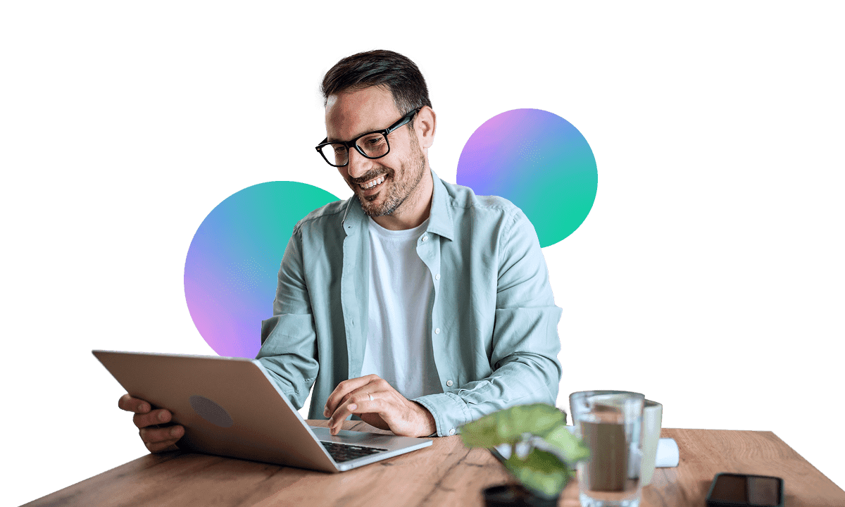 Smiling man wearing glasses and a casual shirt, looking at a laptop.